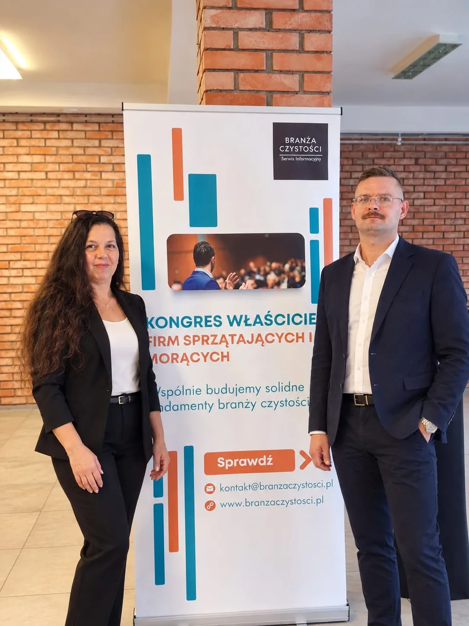 Dwie osoby przy banerze Kongresu Właścicieli Firm Sprzątających i Piorących