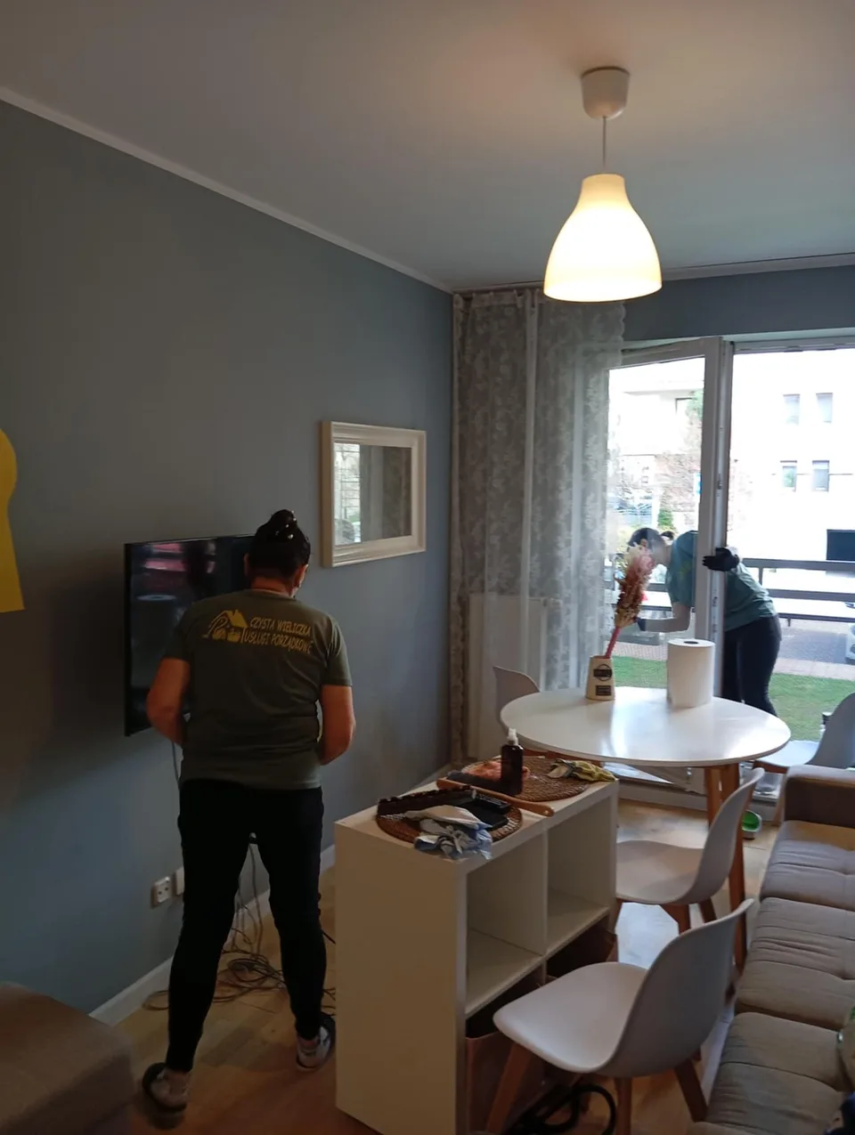 Dwie osoby z ekipy sprzątają salon z częścią jadalnianą